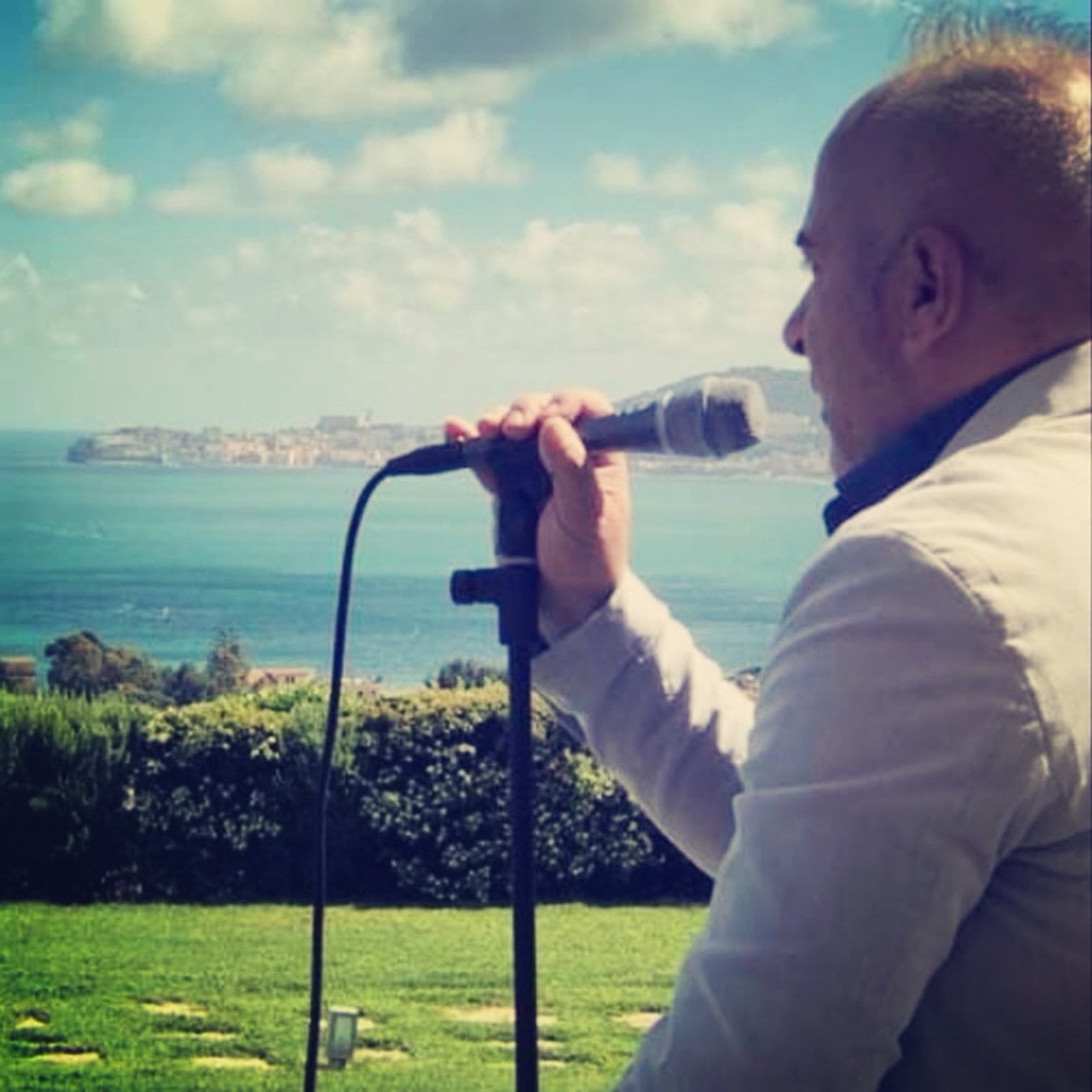 Massimiliano Di Vanni canta con il microfono davanti al golfo e al promontorio di Gaeta